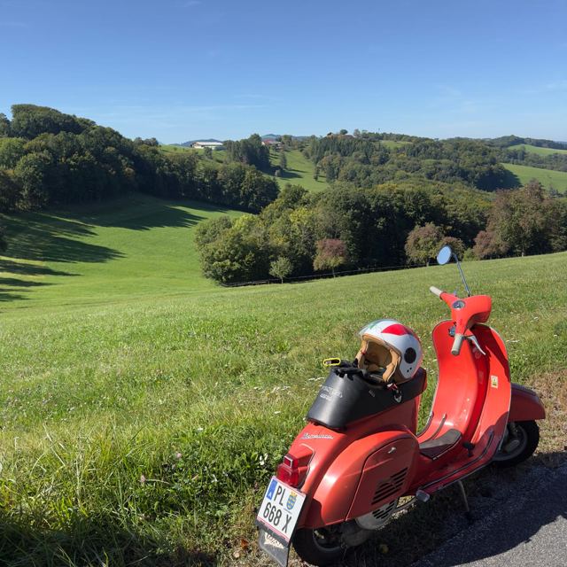 Rote Vespa vor hügeliger Landschaft